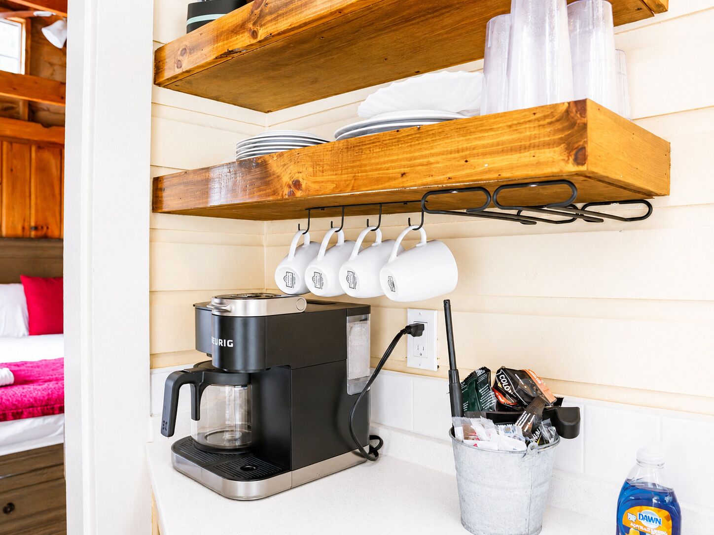 Et tekøkken med kaffemaskine, krus og en bestikholder.