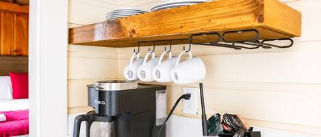 Et tekøkken med kaffemaskine, krus og en bestikholder.