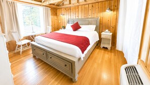 Une chambre aux murs lambrissés, comprenant un lit, des tables de chevet, une chaise et un ventilateur de plafond.