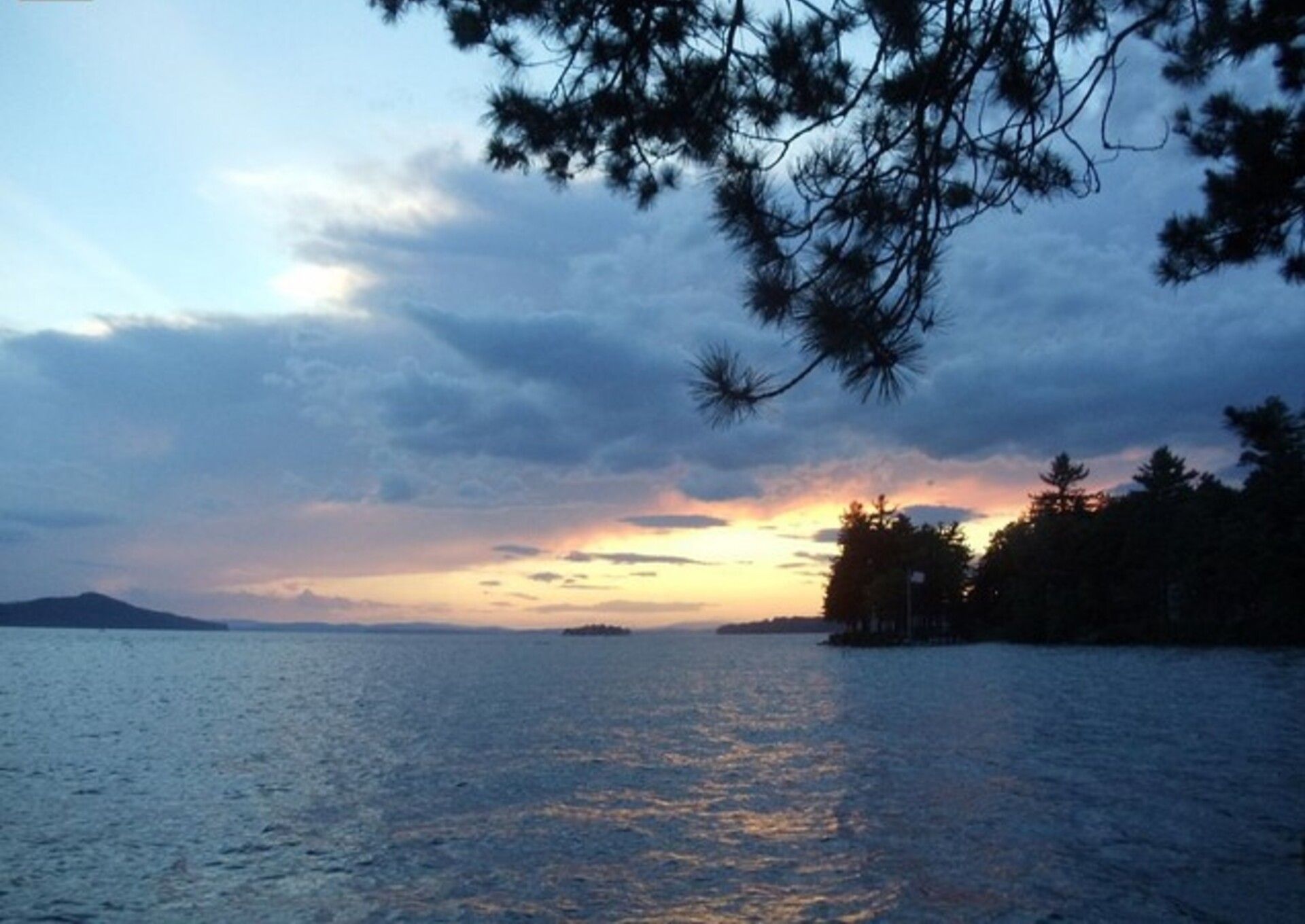 A sunset over a calm body of water with a distant shoreline and trees.
