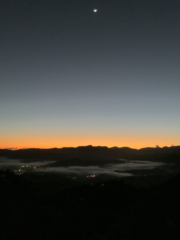 A night sky with a visible moon and a cityscape below, partially obscured by clouds. - La Posada Mountain Retreat in the Heart of Puerto Rico with Exceptional Views (Utuado)