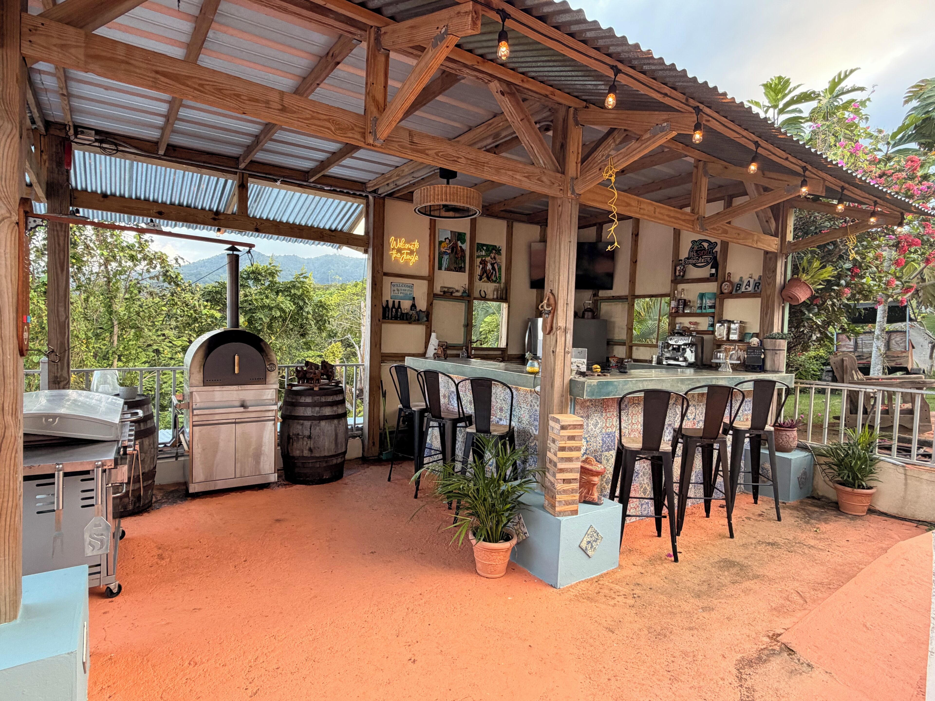 Eine überdachte Terrasse im Freien mit Barbereich, Sitzgelegenheiten und Grill.