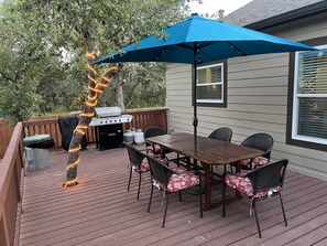 Eine Holzterrasse mit Tisch, Stühlen, einem Grill und einem blauen Sonnenschirm.