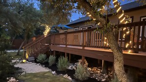 Eine Holzterrasse mit Lichterketten, ein kleiner Garten mit Steinen und Sträuchern sowie ein Haus im Hintergrund.