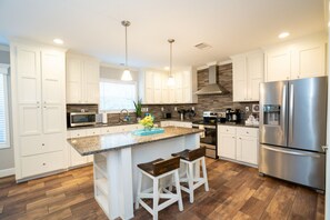 A modern kitchen with white cabinets, a granite countertop, stainless steel appliances, and a central island with bar stools.