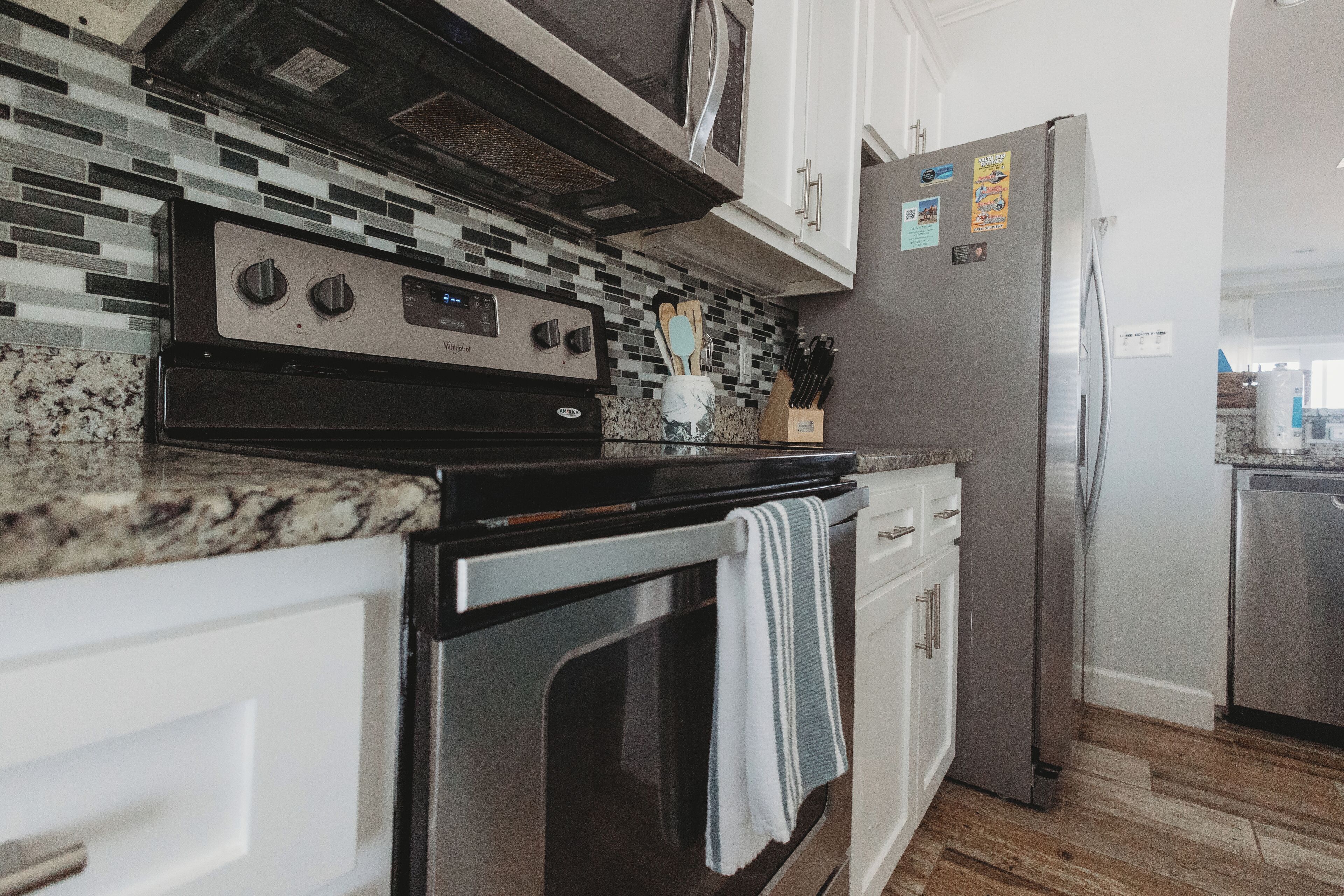 A kitchen with a stainless steel stove, oven, and refrigerator, white cabinets, and a tiled backsplash.