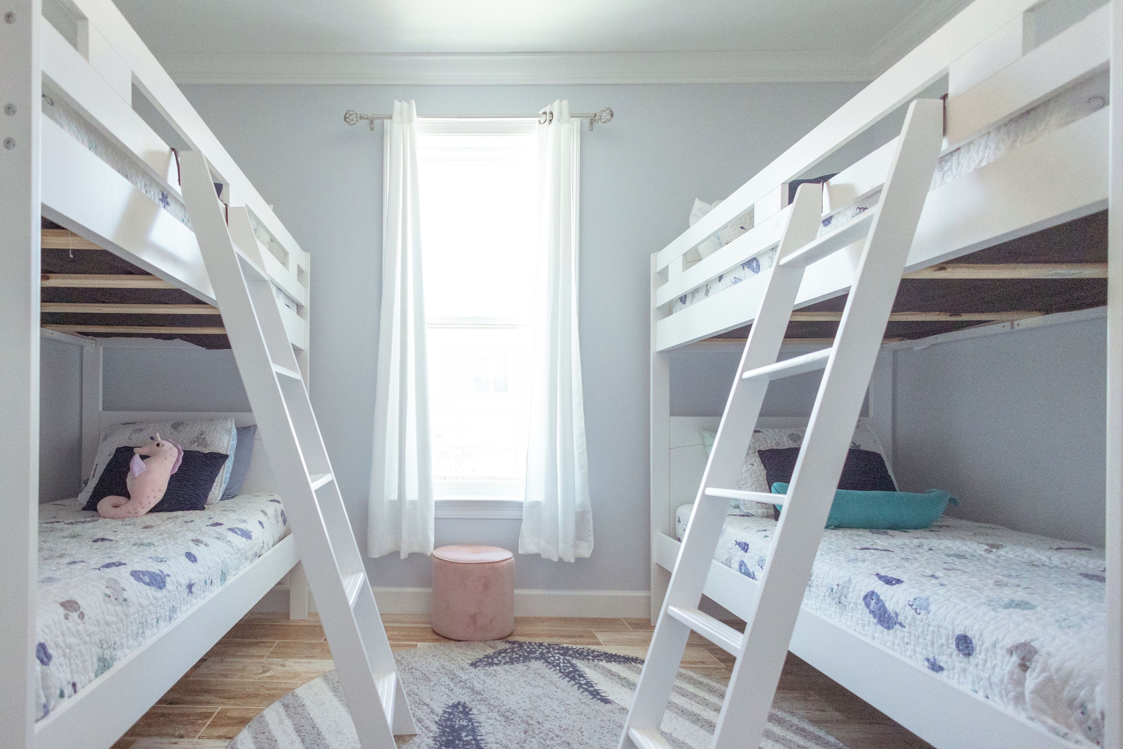 A room with bunk beds, a window with curtains, and a small round stool.