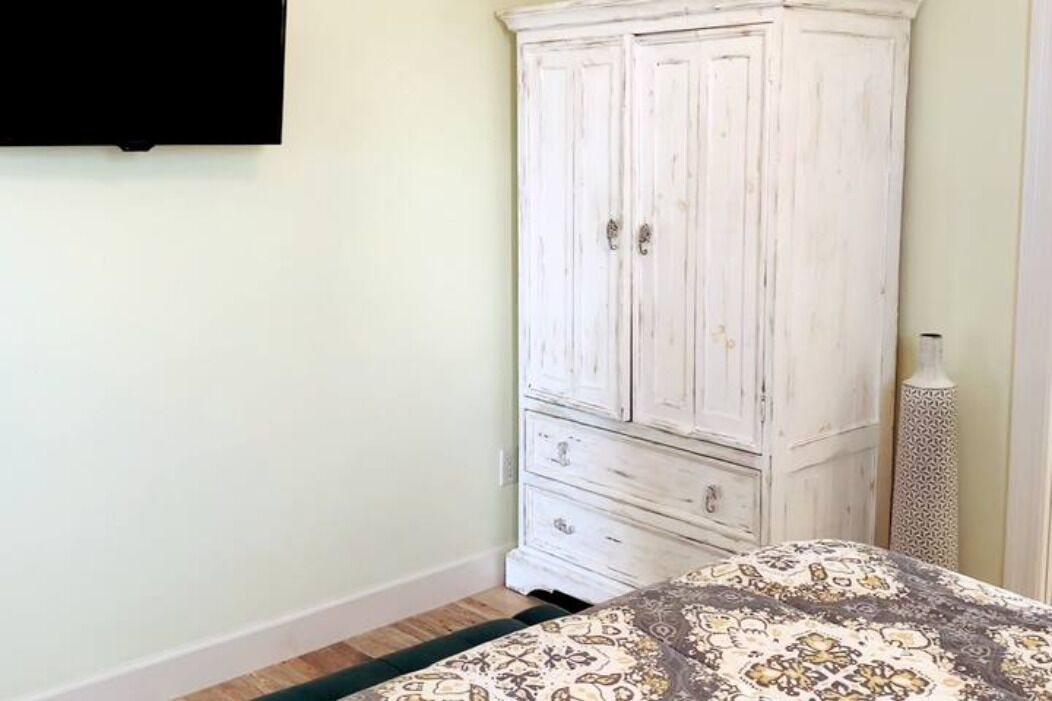 Un dormitorio con cama, un armario blanco y televisor montado en la pared.