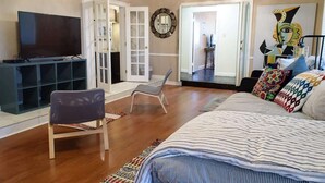 Une chambre à coucher comprenant un lit, une télévision, une chaise, un miroir et une porte donnant sur une autre pièce.