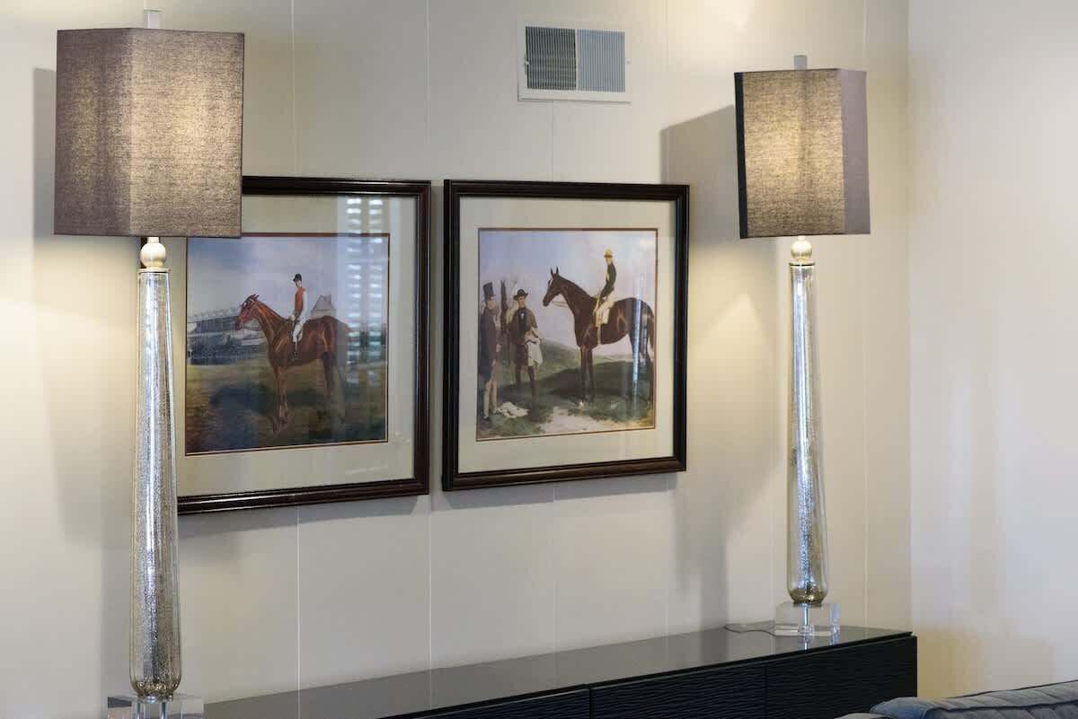 Two framed pictures of horse riders on a wall, flanked by tall lamps with lampshades.