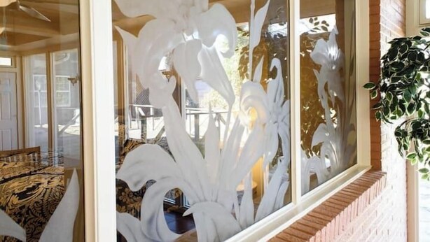 Une pièce dotée d’une grande fenêtre ornée de motifs floraux blancs décoratifs, d’un mur en briques et d’une plante suspendue.