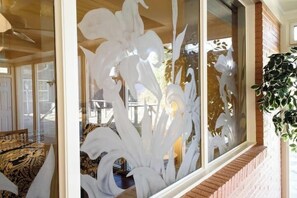 Ein Zimmer mit großem Fenster, das mit weißen floralen Mustern verziert ist, einer Ziegelwand und einer hängenden Pflanze.