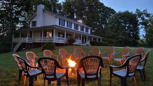 A large house with a porch and multiple chairs arranged around a fire pit. - Restful Rustic Farmhouse on Lake Cumberland (Jamestown)