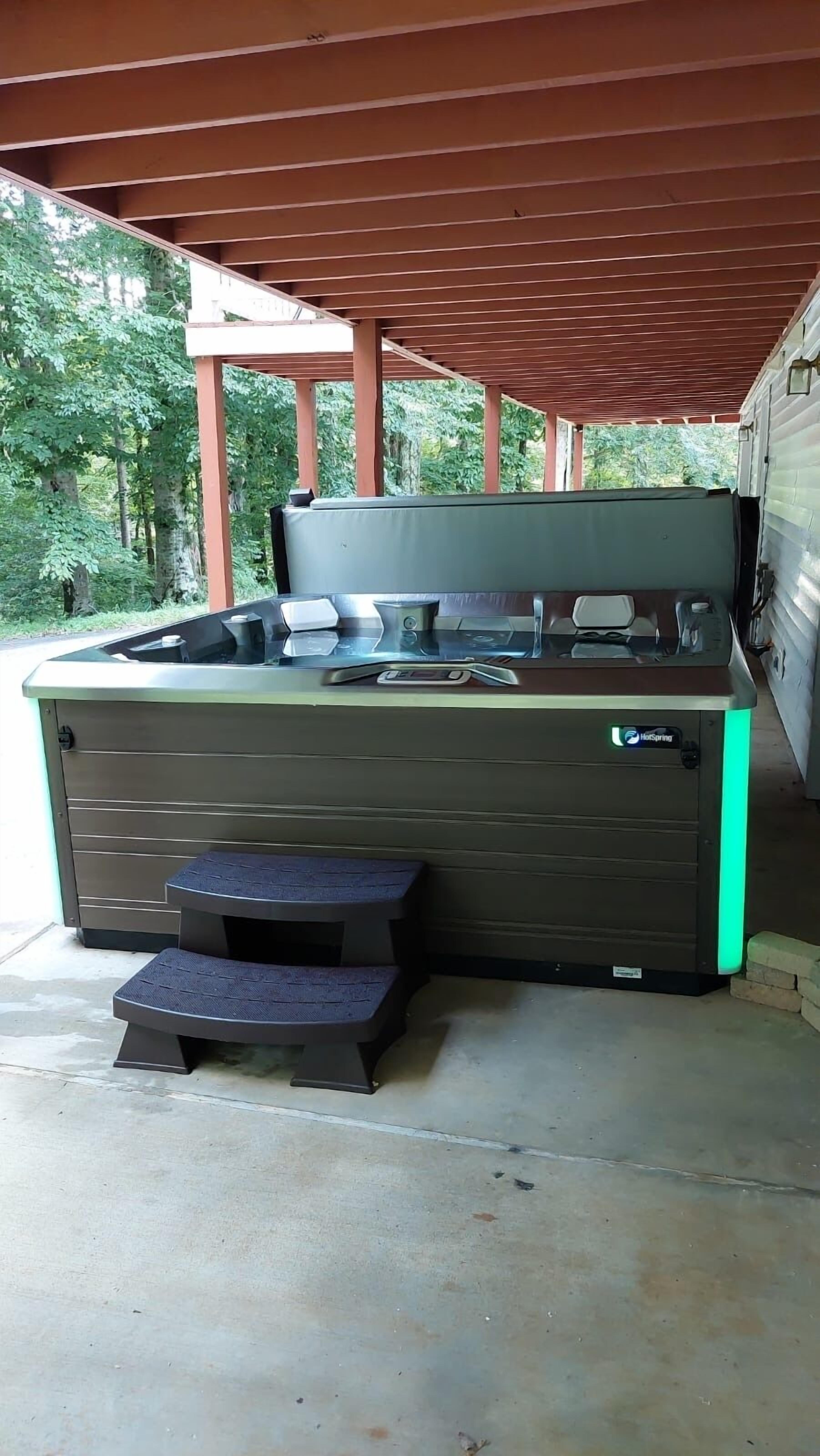 A hot tub with steps and a control panel, located under a covered area with a wooden roof.