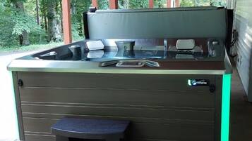 A hot tub with steps and a control panel, located under a covered area with a wooden roof.