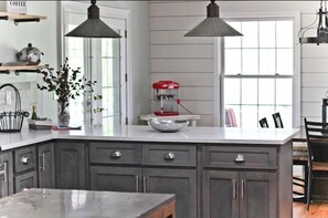 A modern kitchen with a large island, dark cabinets, pendant lighting, and a coffee maker.
