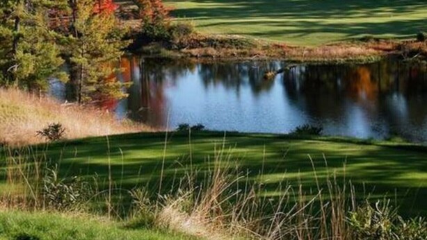 Un parcours de golf avec un étang, entouré d’arbres aux feuilles d’automne.