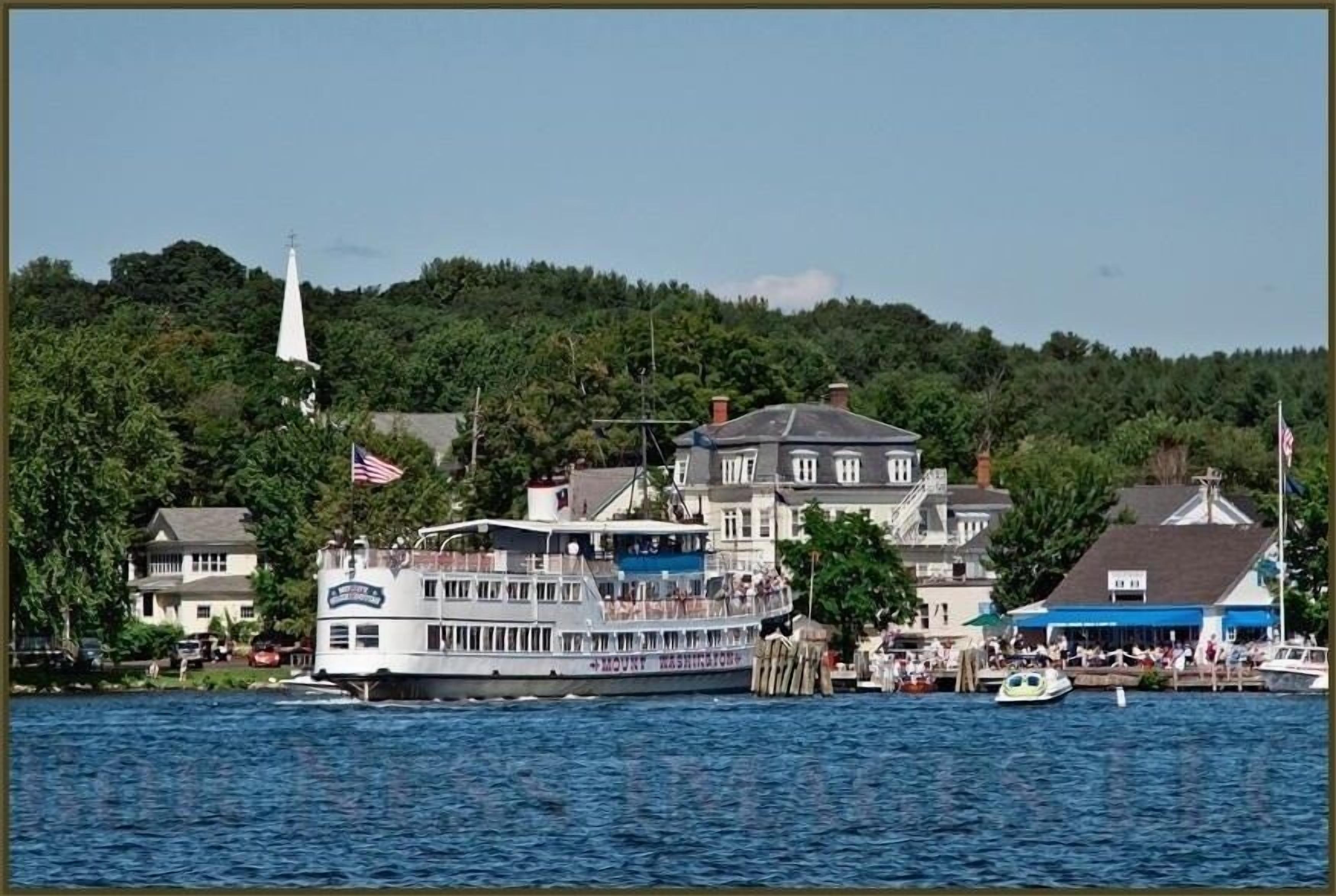 Un hôtel situé au bord de l’eau, avec un grand bâtiment blanc, un quai et une colline boisée en arrière-plan.
