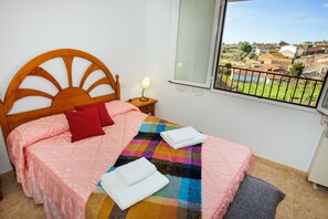 Une chambre à coucher avec un lit, une table de chevet, une fenêtre donnant sur un village et une balustrade de balcon.
