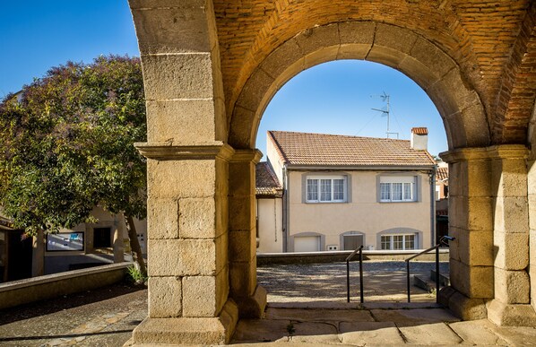 Une structure en pierre en forme d’arche mène à un bâtiment doté d’un toit en tuiles et d’une antenne visible.