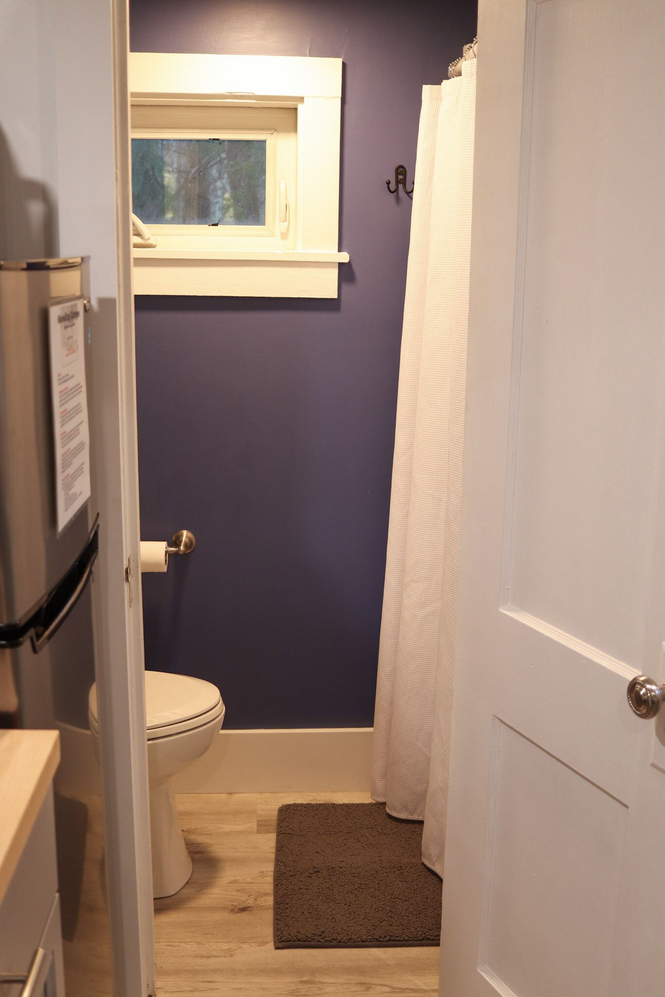 A bathroom with a toilet, a window, a shower curtain, and a door.
