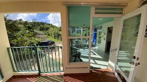 Une pièce dotée d’une porte-fenêtre coulissante donnant sur un balcon avec vue sur une route et un espace verdoyant.
