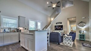 A spacious kitchen with a central island, a dining area with a blue sofa, and a staircase leading to an upper level.