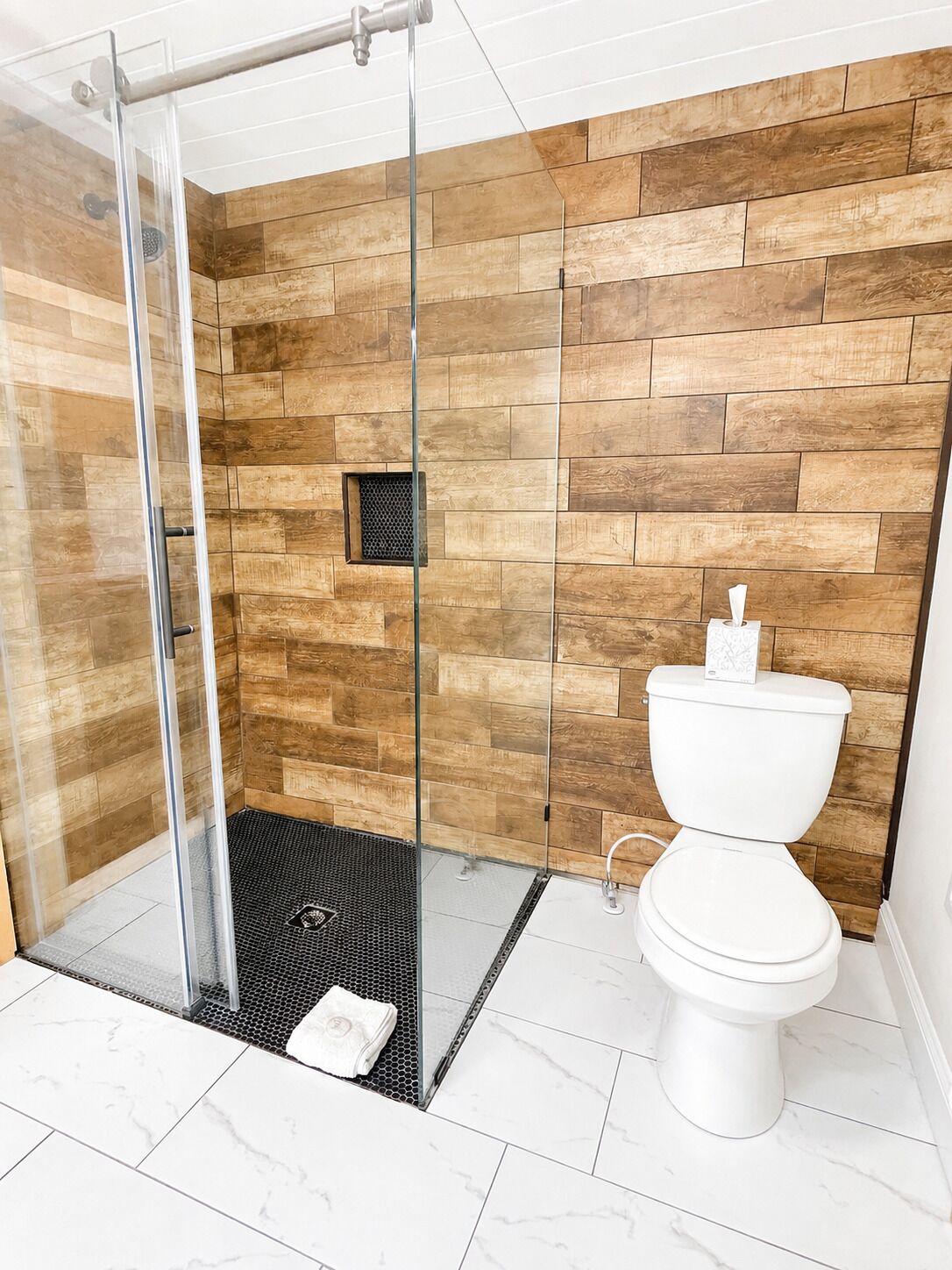 Et moderne badeværelse med glasvægs brusebad, toilet og trævægsdesign.