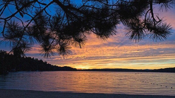 Rauhallinen näkymä järvelle auringonlaskun aikaan, jossa näkyy puiden siluetti ja tyyni vedenpinta.