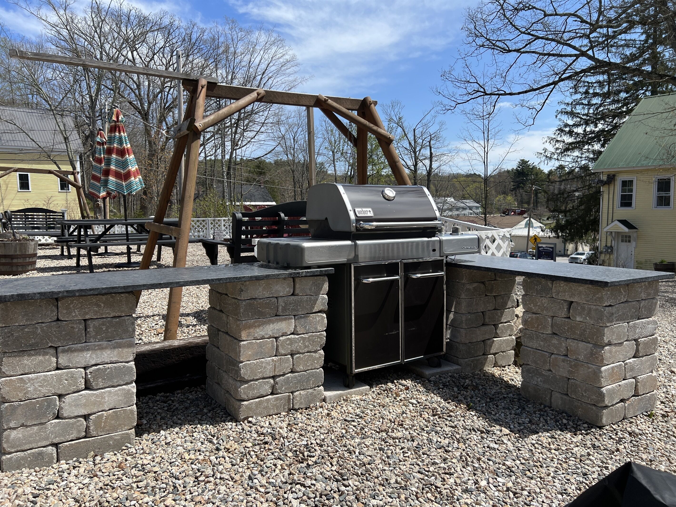 An outdoor barbecue area with a grill, stone walls, and a swing set.
