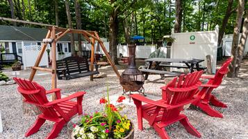 A patio area with red Adirondack chairs, a swing set, a picnic table, and a fire pit.