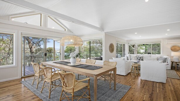 A spacious living area with a dining table, wicker chairs, and a white sofa. - Bush Retreat with Bayviews at Pretty Beach (HARDYS BAY)