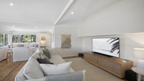 A modern living room with a large flat-screen TV, a sofa set, and a wooden entertainment unit. - Bush Retreat with Bayviews at Pretty Beach (HARDYS BAY)