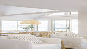 A bright, airy room with large windows, wicker furniture, and a white color scheme. - Bush Retreat with Bayviews at Pretty Beach (HARDYS BAY)