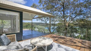 A deck with a table and chairs, overlooking a scenic landscape with trees and a body of water. - Bush Retreat with Bayviews at Pretty Beach (HARDYS BAY)