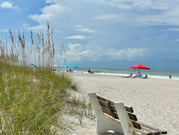 Ein Strand mit einer Bank, einem roten Sonnenschirm und einem blauen Zelt.