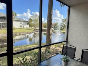 Ein Zimmer mit großem Fenster und Blick auf einen Teich, einem Tisch mit Stühlen und einer Zimmerpflanze.