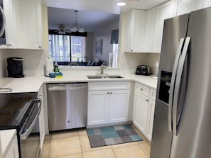A modern kitchen with white cabinets, stainless steel appliances, a dishwasher, and a refrigerator. - JD-near Beaches and IMG, Pool, Tennis, Pickleball, Shorewalk condo 2 Bedroom/2 Bath lake view (Bradenton)