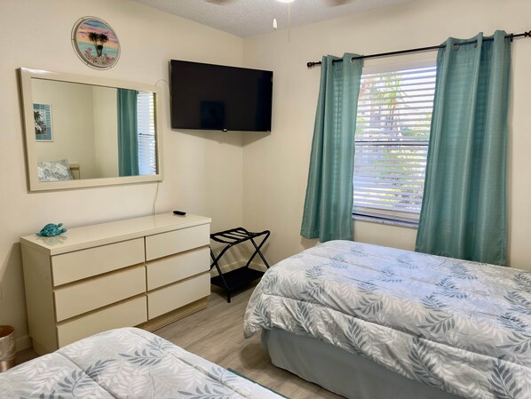 Un dormitorio con cama, cómoda, televisor, ventana con cortinas y espejo.