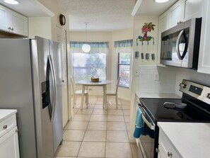 A kitchen with a refrigerator, stove, microwave, and a dining table with chairs. - JD-near Beaches and IMG, Pool, Tennis, Pickleball, Shorewalk condo 2 Bedroom/2 Bath lake view (Bradenton)