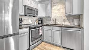 A modern kitchen with stainless steel appliances, white cabinetry, and a stone backsplash. - Beach House just steps from Sun & Fun! (North Palm Beach)
