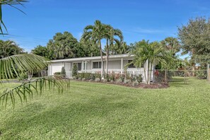 A single-story house with a front porch, surrounded by a well-maintained lawn and palm trees.
