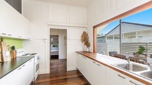 A modern kitchen with white cabinetry, a wooden countertop, and a large window overlooking a backyard. - High Three - Charming Beachside Retreat in the Heart of Yamba - Holiday Yamba (Yamba)