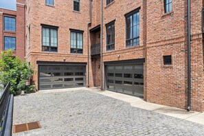 A brick building with two garage doors, a paved courtyard, and a metal fence. - Nashville WeHo Escape | Walk to Bars & Dining (Nashville)
