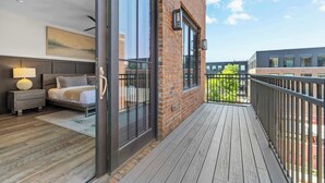A modern bedroom with a large bed, bedside table, and a view of the city through floor-to-ceiling windows.