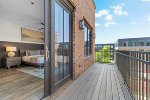 A modern bedroom with a large bed, bedside table, and a view of the city through floor-to-ceiling windows.