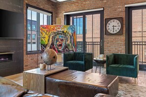 A room with brick walls, large windows, a fireplace, a clock, and a colorful abstract painting. - Nashville WeHo Escape | Walk to Bars & Dining (Nashville)