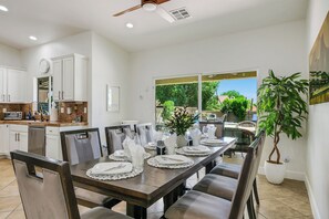 A dining area with a table set for four, chairs, a ceiling fan, and a potted plant.
