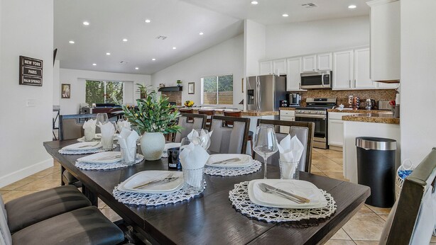A modern kitchen with white cabinets, a stainless steel refrigerator, and a dining area set with white tableware.