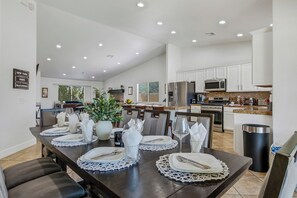 Una cocina moderna con armarios blancos, un refrigerador de acero inoxidable y una zona de comedor con vajilla blanca.